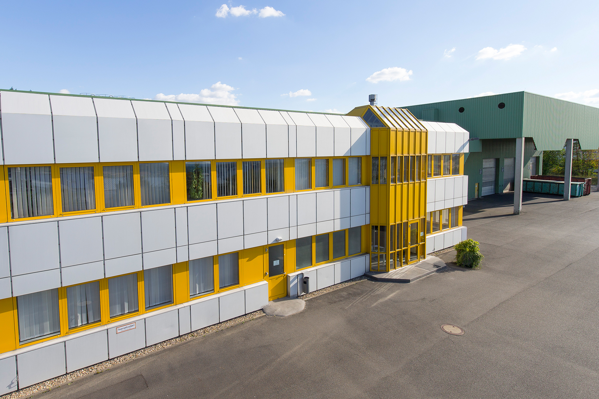 Firmengebäude mit gelber Fensterreihe und grüner Lagerhalle